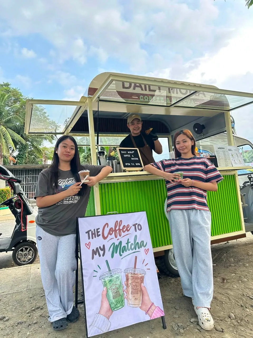 Two guests holding drinks in front of the Daily Moka coffee cart